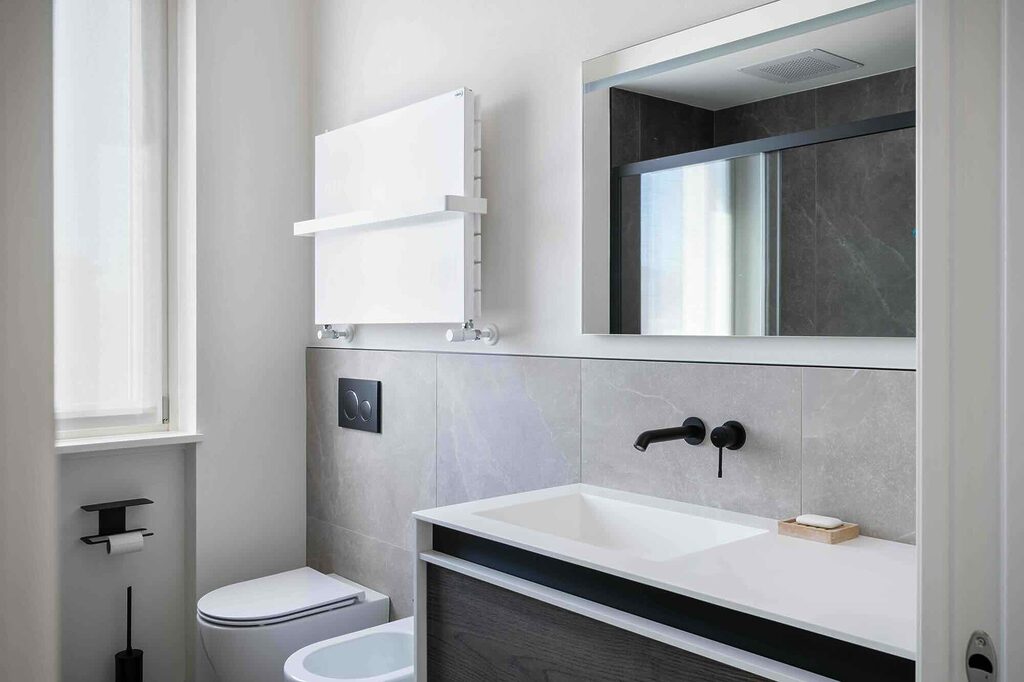 Foto di un bagno moderno ristrutturato con lavabo sospeso, mobile in legno scuro, rubinetteria nera opaca, piastrelle in gres grigio, termoarredo bianco con mensola e specchio con vista sulla doccia.