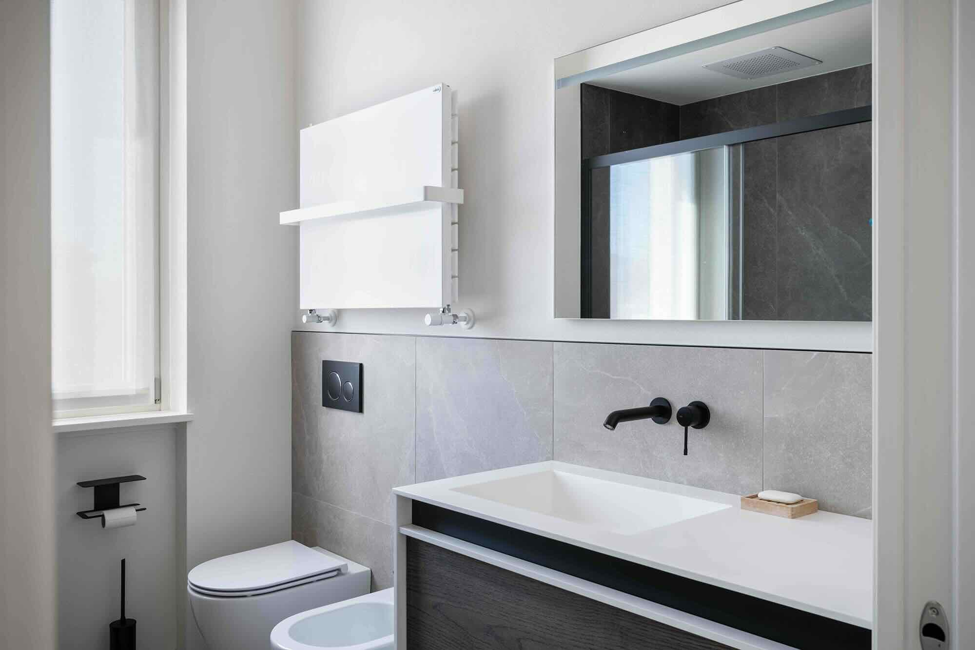 Foto di un bagno moderno ristrutturato con lavabo sospeso, mobile in legno scuro, rubinetteria nera opaca, piastrelle in gres grigio, termoarredo bianco con mensola e specchio con vista sulla doccia.