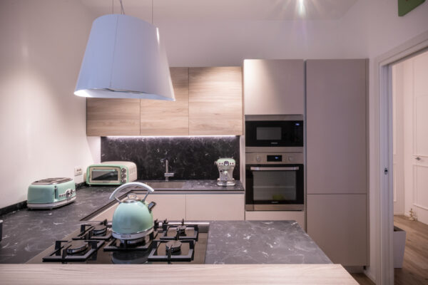 Cucina dopo la ristrutturazione con piano nero marmorizzato, mobili chiari e accessori verde menta