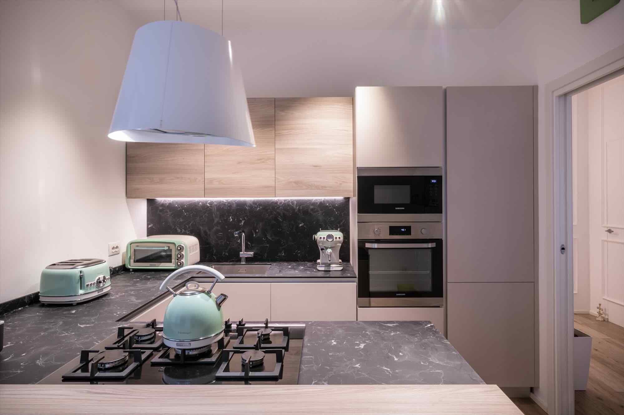 Cucina dopo la ristrutturazione con piano nero marmorizzato, mobili chiari e accessori verde menta